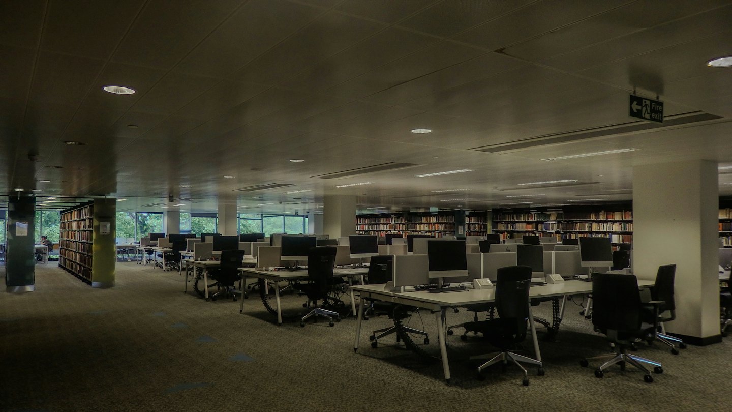 Puestos de trabajo de ordenador vacíos en una biblioteca moderna con libros en las paredes.